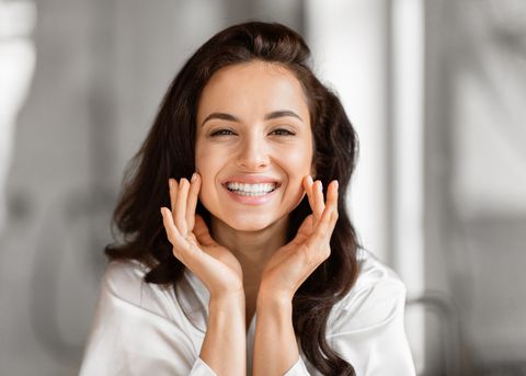 Smiling woman in a white spa robe with her hands framing her glowing skin